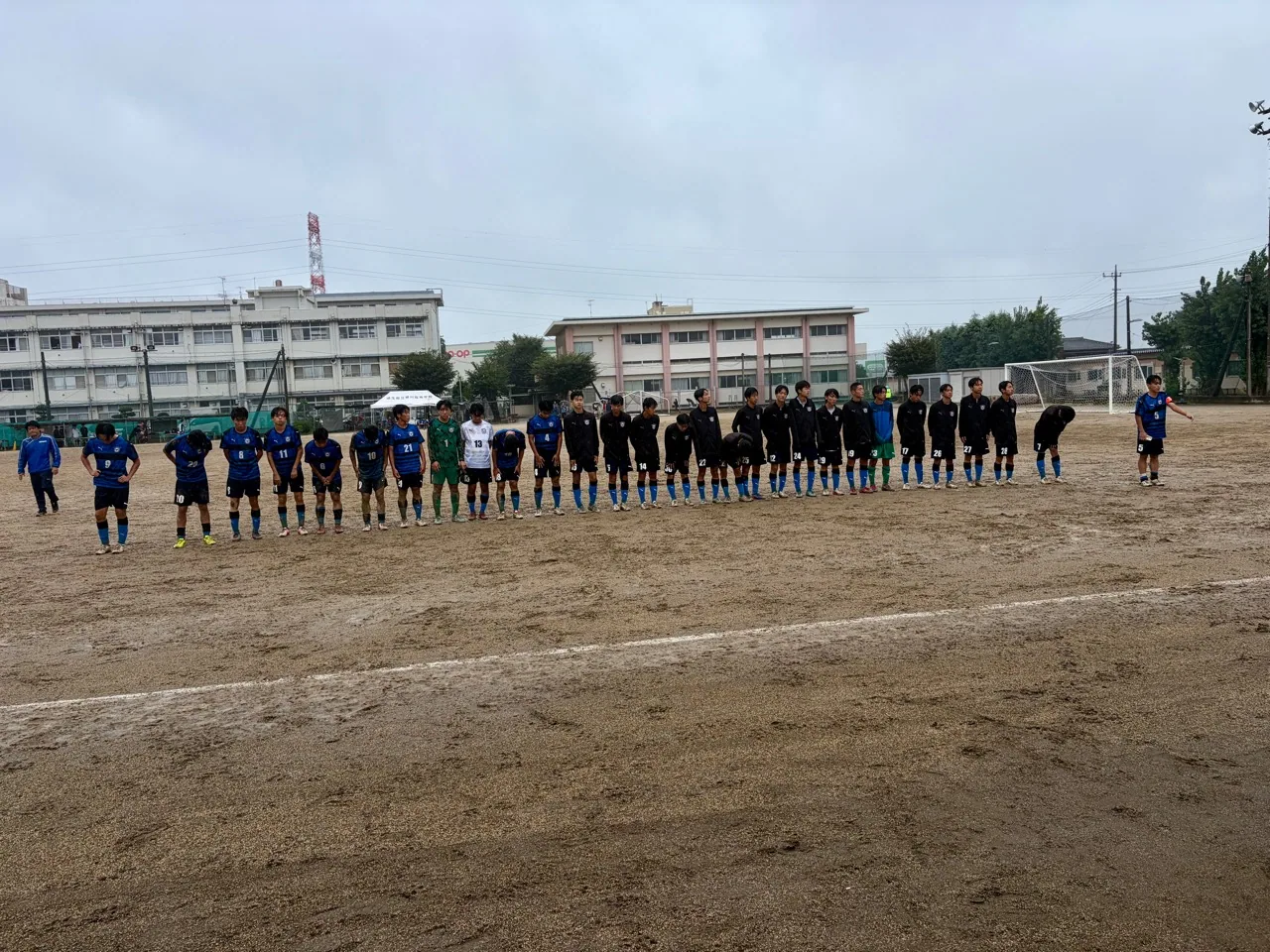 雨のグラウンドで試合後に整列する高校サッカーの選手たち