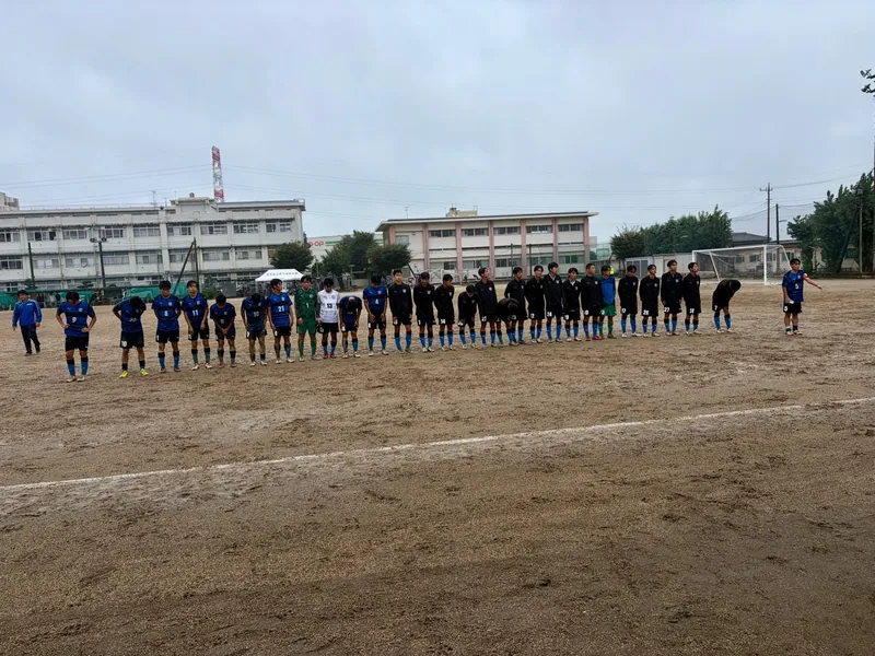 雨のグラウンドで試合後に整列する高校サッカーの選手たち